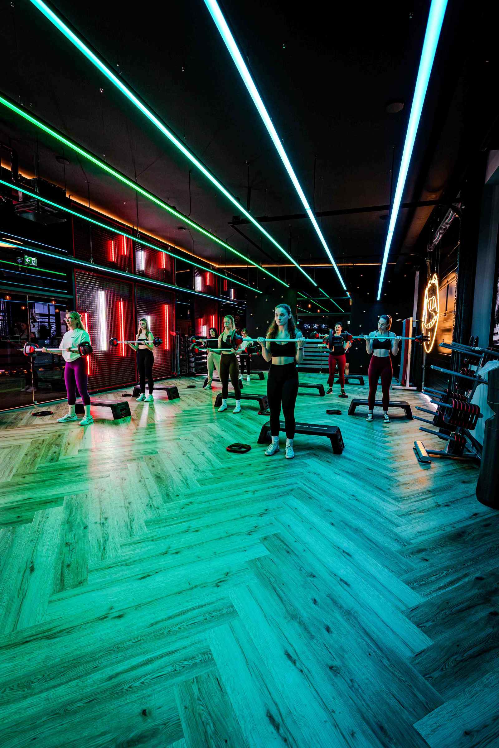 Gruppentraining mit Langhanteln bei GymOne unter grünem und rotem Neonlicht