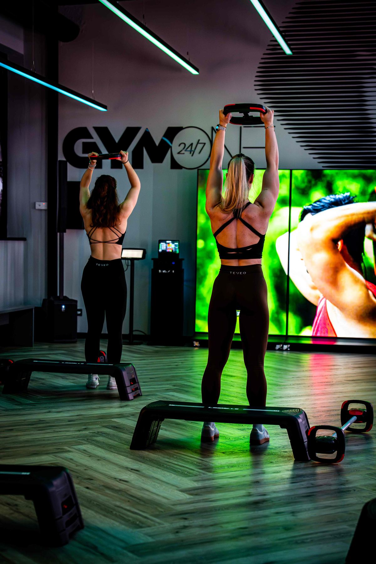 Mitglieder beim Step-Training mit Widerstandsbändern vor der GymOne-Wand und LED-Wall