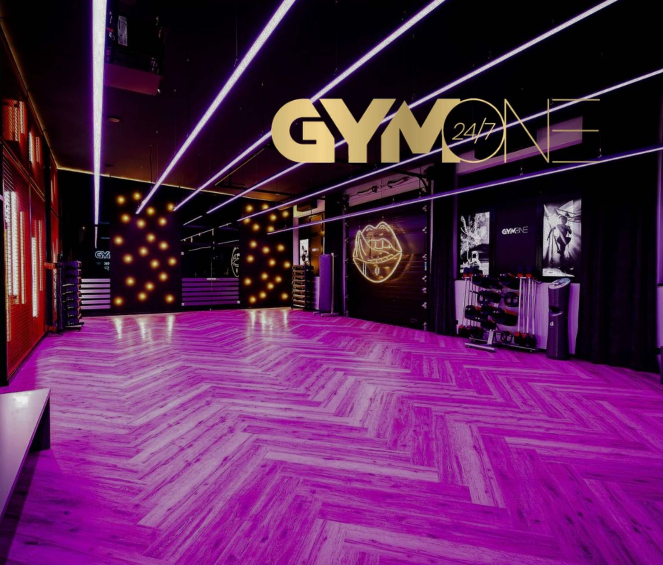 Trainingsbereich von GymOne mit lila schimmerndem Fischgrätparkett, goldenen Lichterinstallationen und dem GymOne-24/7-Logo
