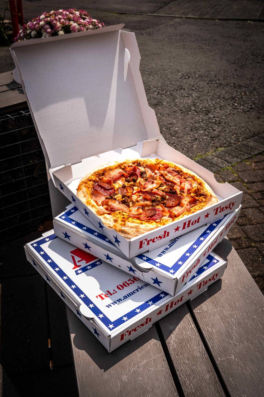 Gestapelte Pizzakartons von Sylvie's American Pizza, oben eine frisch geöffnete Pizza